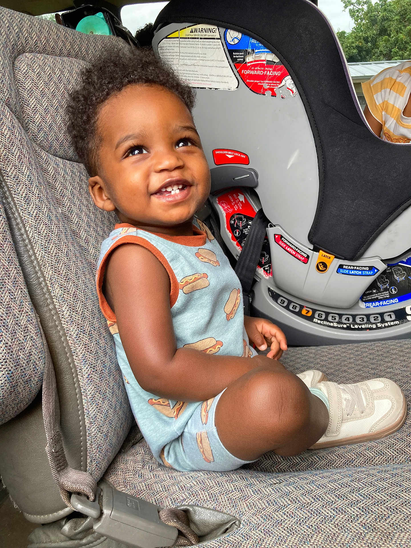 Anthony joined the competition — help win amazing prizes! toddler, child, smiling, car_seat, seatbelt, clothing, hot_dog_print, sneakers, happy, portrait, indoor, seat, person, curly_hair, cute, looking_up, baby, feet, car_interior, safety