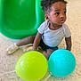 toddler, child, balloons, yellow_balloon, blue_balloon, green_slide, curly_hair, gray_shirt, black_shorts, indoor, playground, floor, speckled_floor, sitting, looking_away, shoes, casual_clothing, young_child, play, daylight