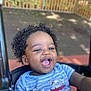 child, toddler, smiling, curly_hair, blue_shirt, mickey_mouse, outdoor, stroller, happy, baby, person, clothing, playful, laughing, cute, seat, daylight, expression, portrait, fun