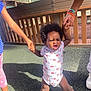 toddler, child, holding_hands, playground, outdoor, determined, sunlight, footwear, clothing, person, support, expression, hair, legs, hand, fence, shadow, sneakers, ground, daytime