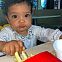 Kaïna a rejoint le concours — aidez-le/la à gagner de superbes lots ! toddler, child, fries, food, table, red_container, curly_hair, indoor, restaurant, white_clothing, collar, hand, face, eyes, person, eating, baby, cute, expression, casual
