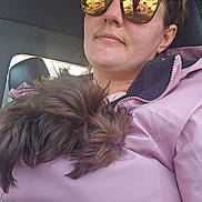 Sadie May is registered to the contest to win money with this photo: person, dog, jacket, sunglasses, reflection, car, seat, nose_ring, pet, fur, closeup, pink, cozy, indoor, casual, portrait, resting, animal, companion, transportation