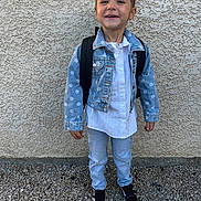Zoé participe au concours pour gagner de l'argent avec cette photo : child, denim_jacket, backpack, jeans, shoes, gravel, wall, smiling, standing, outdoor, casual_clothing, portrait, young, happy, fashion, person, light, texture, full_body, daylight