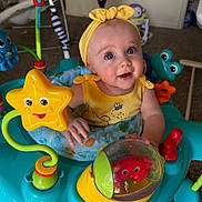 Elsie is registered to the contest to win money with this photo: activity_station, baby, big_eyes, bouncy_seat, carpet, child, colorful_toys, crab_toy, cute_expression, frog_toy, hands, indoor, infant, playtime, portrait, seat, smile, star_toy, yellow_dress, yellow_headband