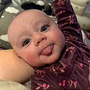 Elsie joined the competition — help win amazing prizes! baby, infant, child, face, eyes, tongue, eyelashes, rosy_cheeks, pajamas, floral_pattern, blanket, bed, arm, hand, closeup, portrait, candid, home_interior, playful_expression, soft_lighting