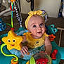 Elsie joined the competition — help win amazing prizes! activity_center, adorable, baby, blue_eyes, carpet, clothing, colorful, crab_toy, fan, frog_toy, headband, indoor, infant, jumper, playtime, sitting, smile, star_toy, toy, yellow_headband