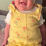 Cali is registered to the contest to win money with this photo: baby, infant, child, smiling, headband, bow, yellow_romper, floral_pattern, chubby_cheeks, blue_eyes, tongue_out, hands, legs, sitting, portrait, indoor, blanket, crib, person, happy