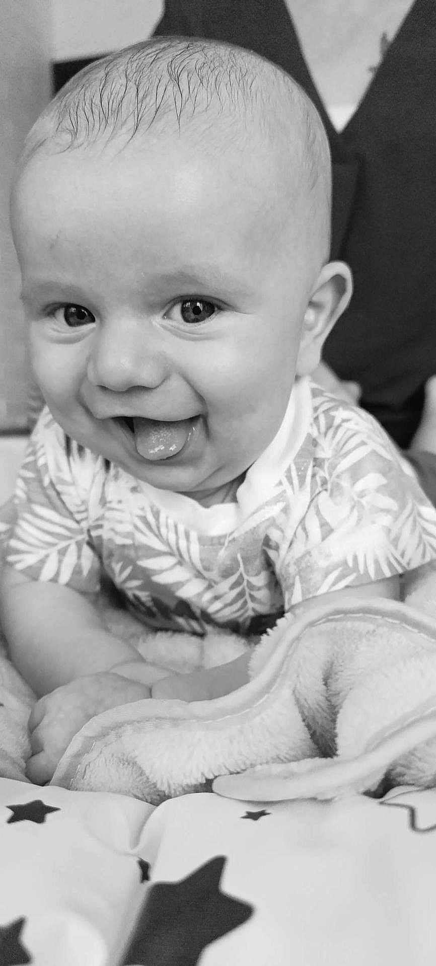 Emile a rejoint le concours — aidez-le/la à gagner de superbes lots ! baby, infant, tongue_out, smiling, black_and_white, blanket, patterned_clothing, cute, face, head, closeup, happy, child, person, indoors, soft_texture, young, playful, eyes, skin