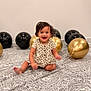 toddler, child, balloons, black_balloons, gold_balloons, carpet, patterned_carpet, smiling, happy, sitting, indoor, wall, ribbons, decoration, celebration, cute, portrait, clothing, short_sleeves, barefoot