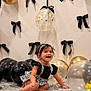baby, child, smiling, balloon, black_bow, gold_balloon, clear_balloon, patterned_cloth, headband, black_top, white_skirt, sitting, celebration, indoor, decor, happy, portrait, cute, person, festive