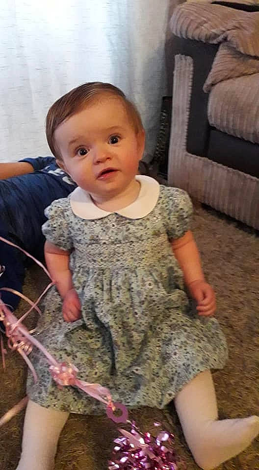 Alyssia is registered to the contest to win money with this photo: arm, baby, cheek, child, dress, leg, person, sitting, skin, smile, thigh, toddler