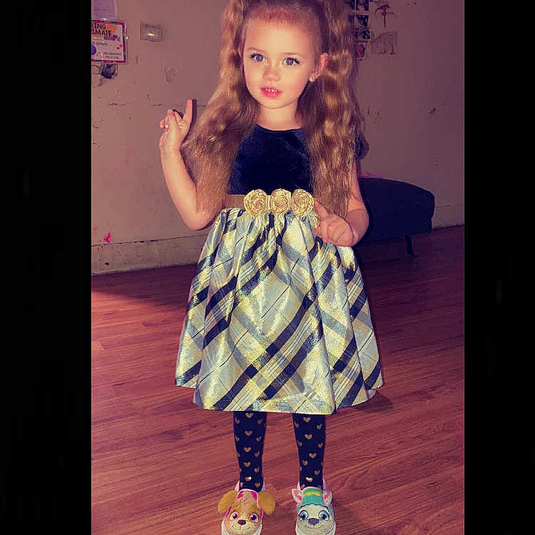 Ava Govero joined the competition — help win amazing prizes! cartoon_slippers, child, cute, decorations, dress, fashion, floor, girl, indoor, long_hair, patterned_dress, peace_sign, pigtails, plaid, slippers, smiling, standing, wall_photos, wooden_floor, young
