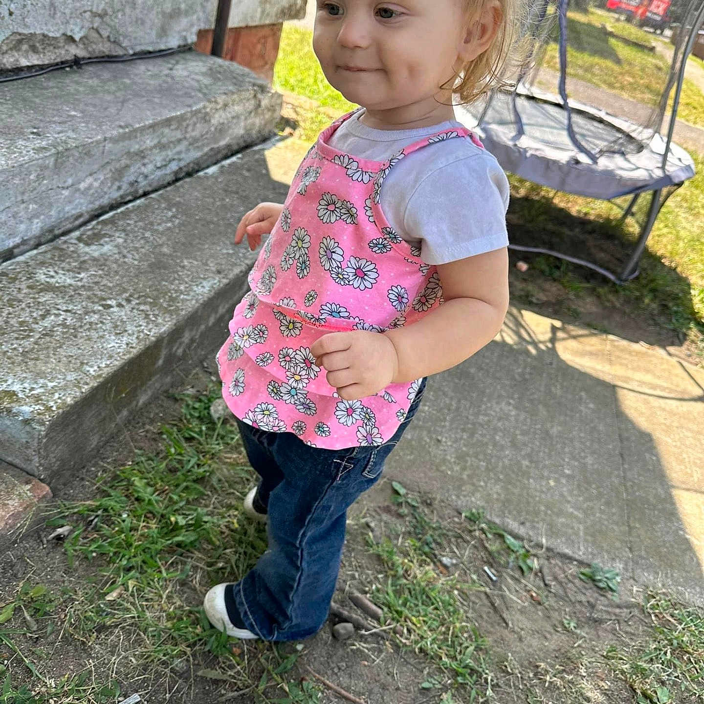 Mia Govero is registered to the contest to win money with this photo: casual_clothing, child, concrete_steps, daytime, dimples, footwear, grass, happy, jeans, nature, outdoor, person, pink_top, playing, side_view, smile, sunlight, toddler, trampoline, young_child