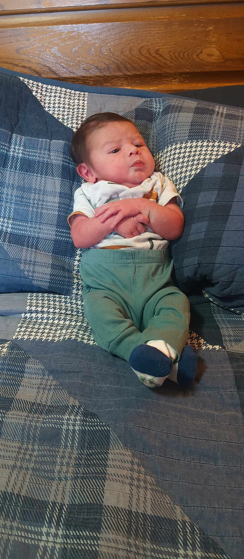 Noah is registered to the contest to win money with this photo: baby, infant, plaid, quilt, bed, wood, headboard, clothing, socks, person, child, indoor, resting, cute, young, portrait, fabric, pattern, cozy, furniture