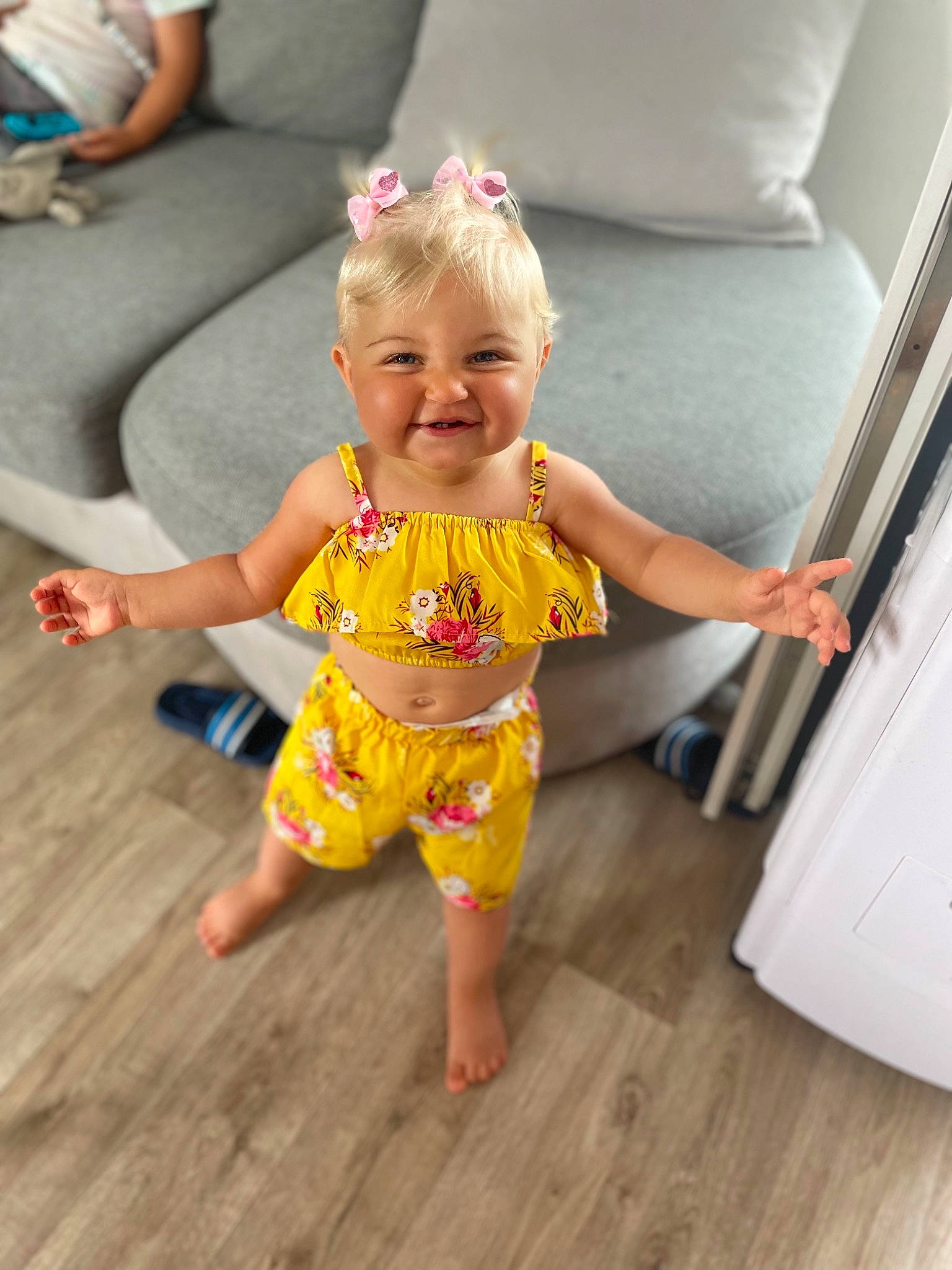 Mia a rejoint le concours — aidez-le/la à gagner de superbes lots ! baby_toddler_clothing, barefoot, child, couch, finger, floor, flooring, foot, fun, happy, hardwood, human_leg, joy, leisure, person, skin, smile, standing, t_shirt, thigh