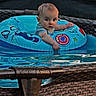 baby, blond_hair, blue, child, daylight, eyes, face, infant, inflatable_ring, outdoor, pool, poolside, portrait, recreation, sitting, summer, swimming, vacation, water, wicker_furniture