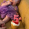 Brighlynn is registered to the contest to win money with this photo: baby, birthday_candle, celebration, child, cupcake, curious, cute, finger_in_mouth, girl, hand, happy, headband, indoor, number_five, pacifier, purple_dress, sitting, smiling, toddler, yellow_chair