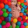 baby, ball_pit, bright_colors, child, childhood, colorful, cute, fun, happy_child, indoor, infant, pacifier, pink_outfit, plastic_balls, play_area, portrait, relaxed, small_child, soft_lighting, toys