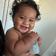 Ermias joined the competition — help win amazing prizes! baby, infant, smiling, curly_hair, bottle, holding, indoor, light_skin, happy, cute, chubby_cheeks, diaper, person, portrait, child, young, expression, hand, face, home