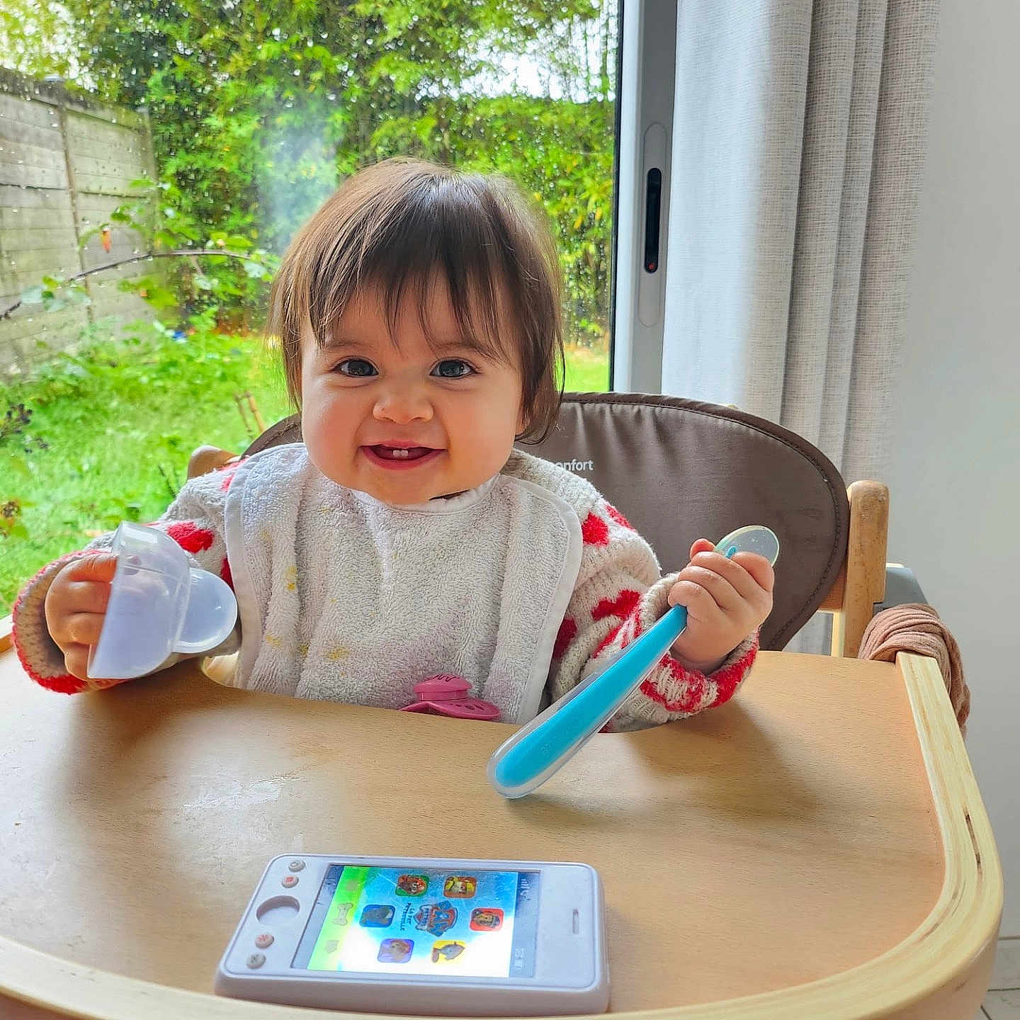 Jolene participe au concours pour gagner de l'argent avec cette photo : baby, bib, child, clothing, curtains, face, greenery, happy, high_chair, home, indoor, person, play, smiling, spoon, table, toddler, toy_phone, window, wooden