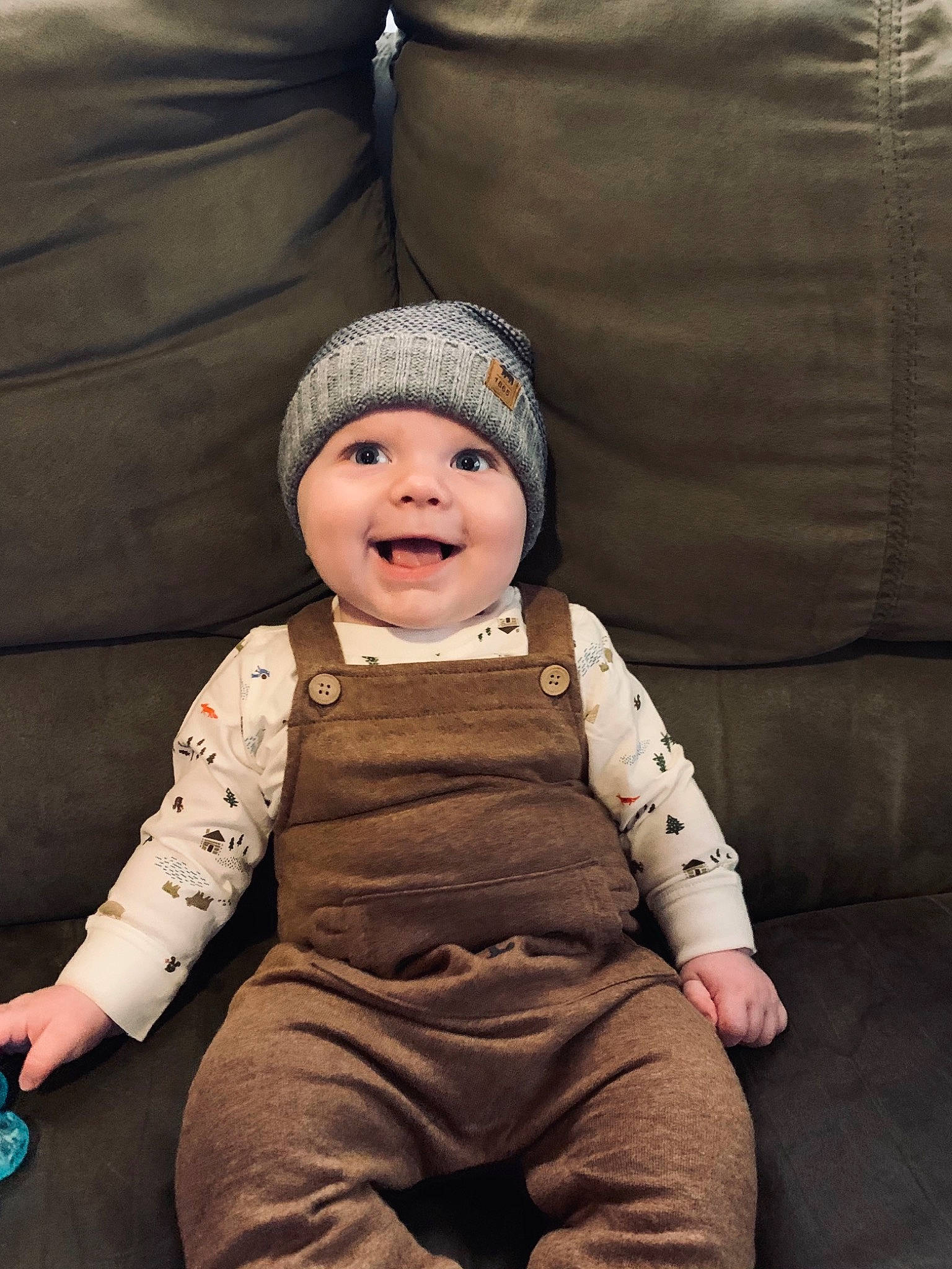 Aaden is registered to the contest to win money with this photo: armrest, baby, baby_laughing, baby_products, baby_toddler_clothing, beanie, bonnet, cheek, child, comfort, headwear, joy, laugh, mouth, nose, overall, person, sitting, sleeve, slipcover