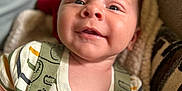 Maverick is registered to the contest to win money with this photo: baby, smiling, infant, close_up, cute, face, child, outdoor, apparel, clothing, animal_print, green, striped_shirt, happy, portrait, young, skin, head, eyes, blanket