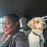 Snowball is registered to the contest to win money with this photo: woman, dog, car, portrait, selfie, curly_fur, fluffy, white_dog, leash, harness, glasses, braid, smiling, seated, vehicle_interior, passenger, companion, pet, daylight, closeup