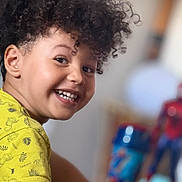 Yanis a rejoint le concours — aidez-le/la à gagner de superbes lots ! child, smiling, curly_hair, yellow_shirt, monkey_print, face, person, indoor, toy, spiderman, cup, background_blur, happy, portrait, playful, kid, closeup, cheerful, casual_clothing, home
