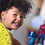 child, smiling, curly_hair, yellow_shirt, monkey_print, face, person, indoor, toy, spiderman, cup, background_blur, happy, portrait, playful, kid, closeup, cheerful, casual_clothing, home