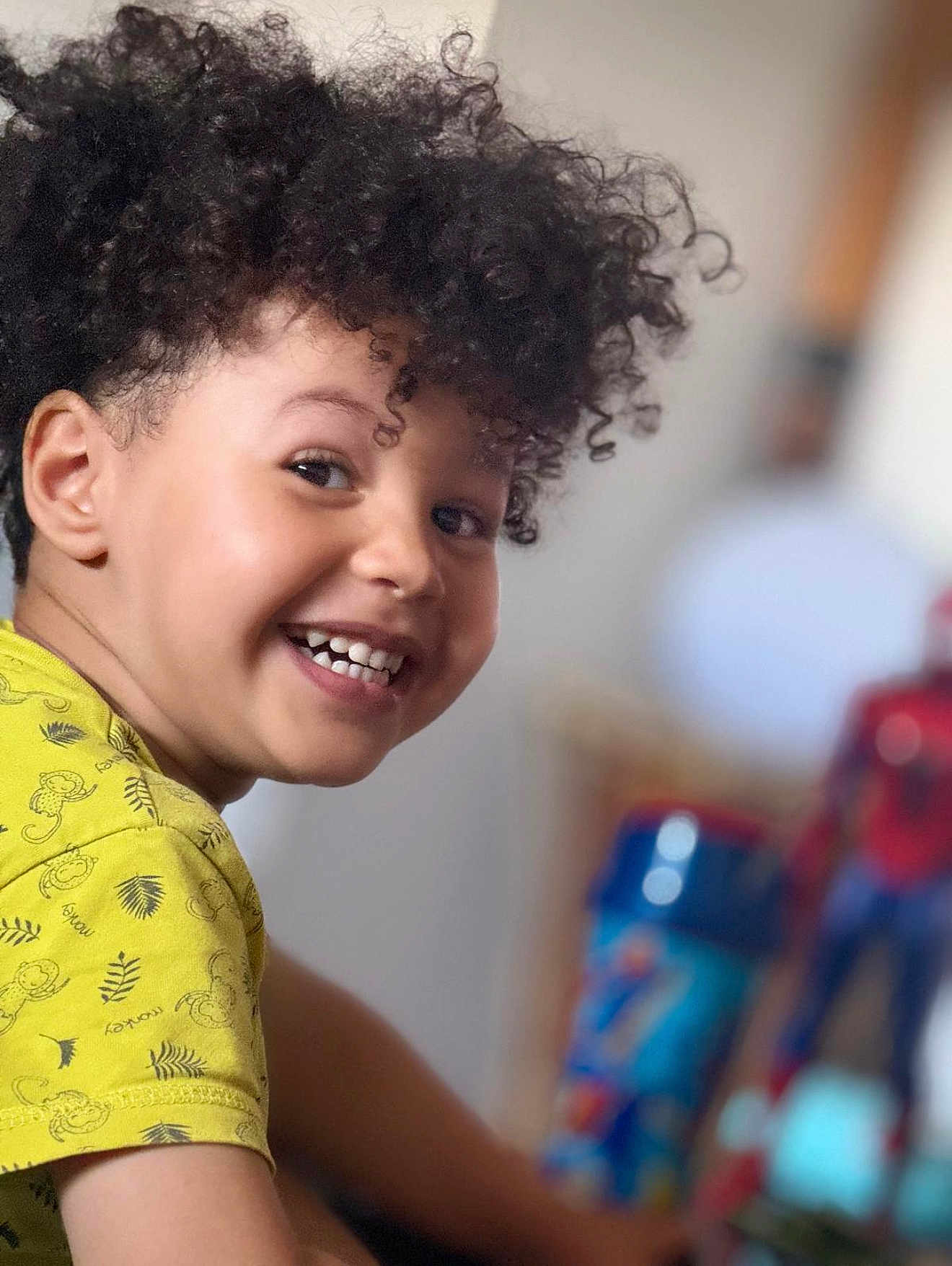 Yanis a rejoint le concours — aidez-le/la à gagner de superbes lots ! child, smiling, curly_hair, yellow_shirt, monkey_print, face, person, indoor, toy, spiderman, cup, background_blur, happy, portrait, playful, kid, closeup, cheerful, casual_clothing, home