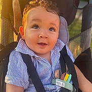 Adam joined the competition — help win amazing prizes! baby, child, close_up, curly_hair, eyes, face, family, golden_hour, happy, harness, infant, outdoor, portrait, seatbelt, sitting, smiling, striped_shirt, stroller, sunlight, vehicle_seat