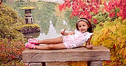 Marwa joined the competition — help win amazing prizes! child, girl, outdoor, garden, autumn, fall_leaves, pond, bench, stone_bench, lantern, japanese_garden, nature, portrait, sitting, reclining, smiling, pink_dress, headband, colorful_shoes, reflection