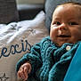 Alexis a rejoint le concours — aidez-le/la à gagner de superbes lots ! baby, child, smiling, knit_sweater, teal, pillow, embroidered, name, alexis, stars, hand, face, indoors, cozy, couch, soft_focus, portrait, cute, happy, infant