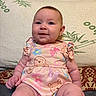 baby, infant, child, portrait, smiling, sitting, pink_outfit, butterfly_pattern, bear_pattern, dress, cushion, sofa, wooden_furniture, indoor, home, cozy, looking_at_camera, round_face, earring, photography