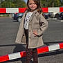 child, girl, standing, pose, coat, jacket, shirt, pants, sneakers, outdoor, parking_lot, barrier, red, white, asphalt, daylight, casual_clothing, smile, long_hair, fashion