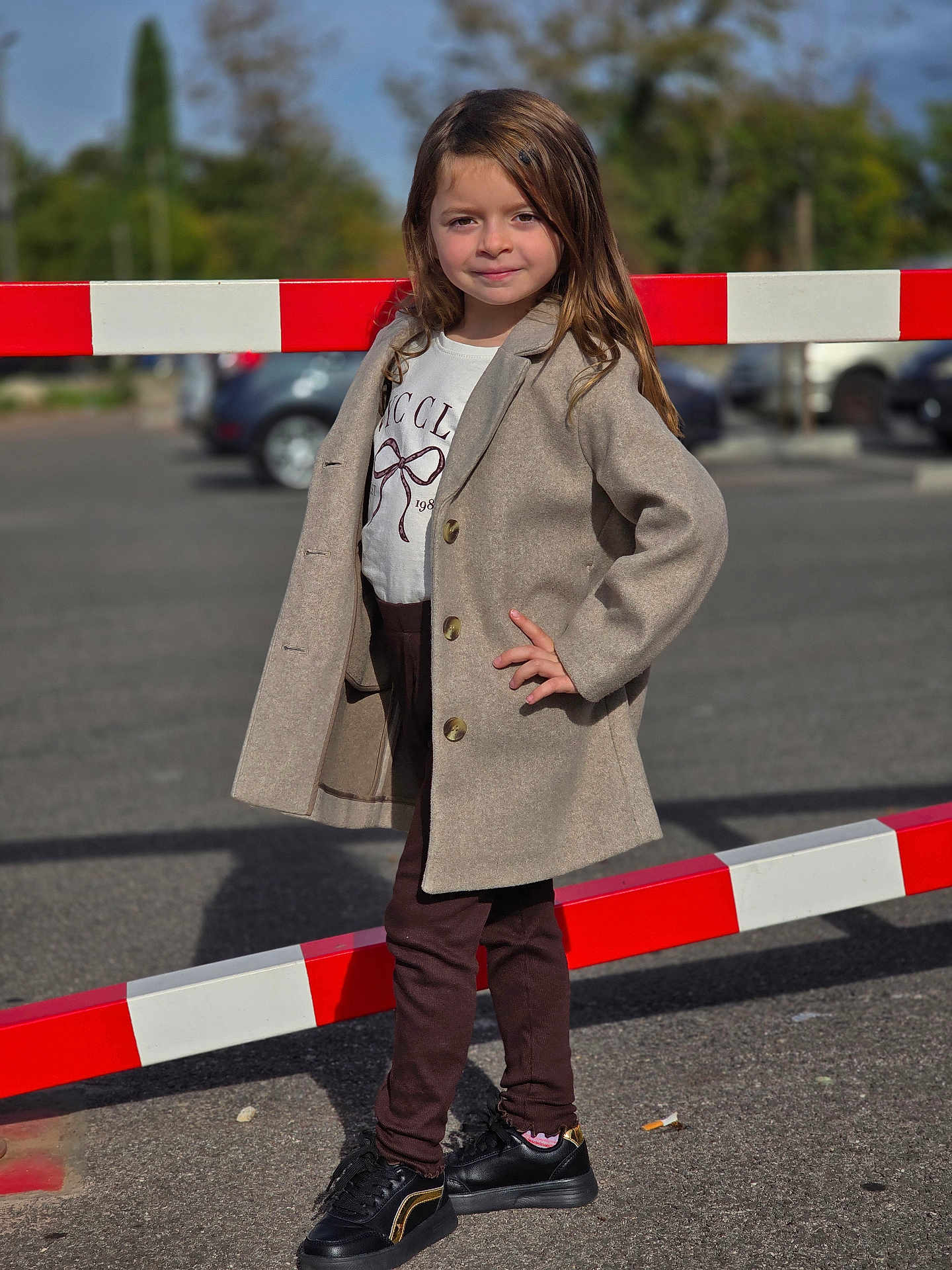 Giulia a rejoint le concours — aidez-le/la à gagner de superbes lots ! child, girl, standing, pose, coat, jacket, shirt, pants, sneakers, outdoor, parking_lot, barrier, red, white, asphalt, daylight, casual_clothing, smile, long_hair, fashion