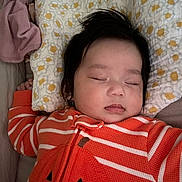 Ivy is registered to the contest to win money with this photo: baby, sleeping, pajamas, orange, striped_clothing, pumpkin_face, pillow, flower_pattern, bed, blanket, child, face, peaceful, indoors, cozy, resting, cute, infant, person, head