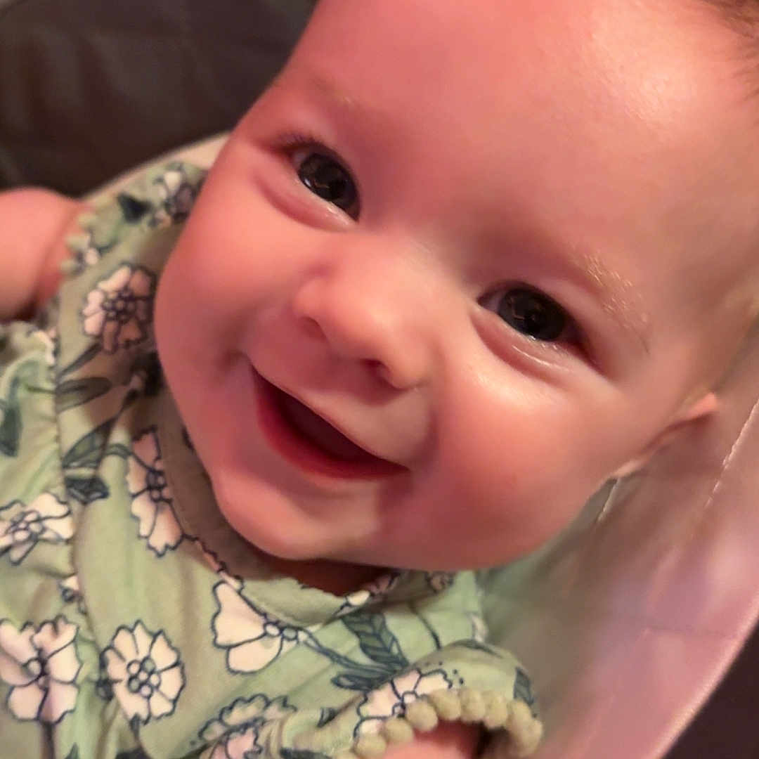 Eliana is registered to the contest to win money with this photo: baby, infant, child, smiling, happy, portrait, close_up, face, eyes, floral_clothing, green_outfit, seated, baby_seat, pink, indoor, cozy, photography, cute, joyful, head