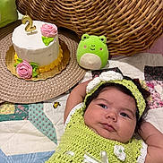 Samira is registered to the contest to win money with this photo: baby, birthday_candle, cake, celebration, child, crocheted_dress, cute, frog_plush, green, headband, indoors, infant, patchwork, pink_rose, plush_toy, portrait, quilt, white_cake, wicker, woven_placemat