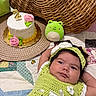 baby, birthday_candle, cake, celebration, child, crocheted_dress, cute, frog_plush, green, headband, indoors, infant, patchwork, pink_rose, plush_toy, portrait, quilt, white_cake, wicker, woven_placemat