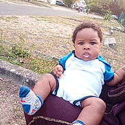Yazid Imran participe au concours pour gagner de l'argent avec cette photo : baby, child, infant, person, outdoor, grass, road, building, sock, clothing, sitting, holding, face, expression, lap, curly_hair, daylight, nature, footwear, sidewalk