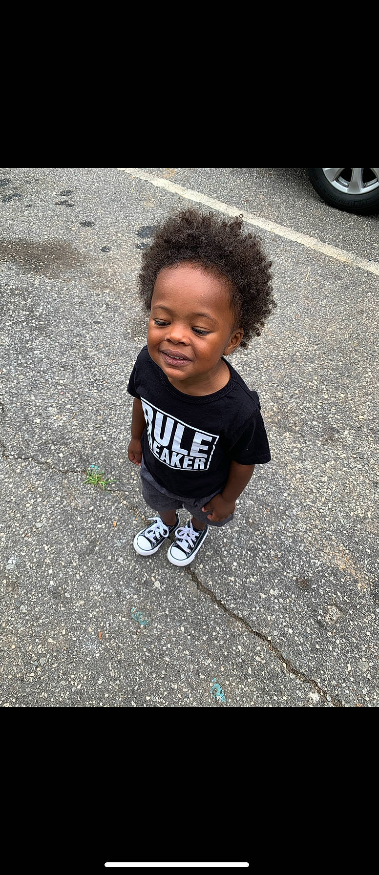 Knox is registered to the contest to win money with this photo: asphalt, automotive_exterior, automotive_tire, baby, baby_toddler_clothing, face, flooring, fun, grass, happy, person, road_surface, sidewalk, smile, soil, t_shirt, tar, tire, toddler, vehicle_door