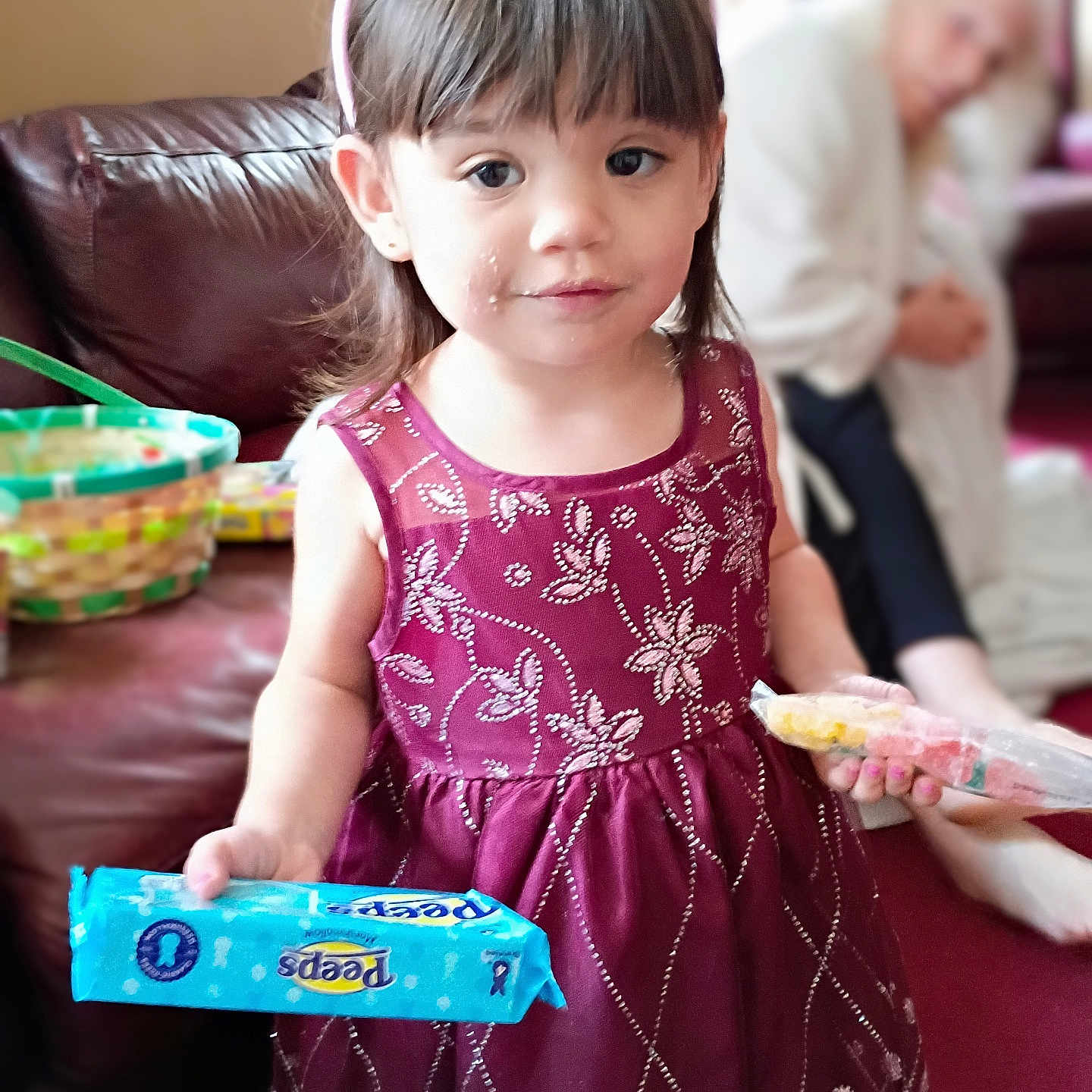 Charlotte is registered to the contest to win money with this photo: child, girl, dress, bunny_ears, snack, food, indoor, couch, person, face, smile, hair, hand, package, purple_dress, carpet, woman, blurred_background, home, cute