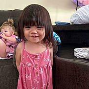 Charlotte joined the competition — help win amazing prizes! child, toddler, girl, pink_dress, smile, indoor, sofa, couch, hair, bangs, furniture, clothing, person, room, curly_hair, pillow, fabric, playful, background, casual