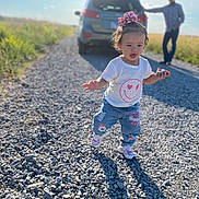 Khilynn is registered to the contest to win money with this photo: toddler, child, gravel_road, rock, pink_bow, white_tshirt, jeans, sneakers, car, man, sunny_day, outdoor, nature, grass, person, walking, shadow, blue_sky, casual, background