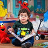 toddler, child, book, sesame_street, elmo, big_bird, cookie_monster, toy, reading, indoor, playtime, radio_flyer, wagon, curly_hair, colorful, floor, smile, clothing, background, happy