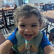 Yeshua joined the competition — help win amazing prizes! toddler, child, smiling, curly_hair, bib, snoopy, woodstock, indoor, restaurant, table, chair, happy, portrait, baby, person, cute, clothing, face, young_child, playful