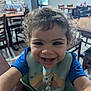 toddler, child, smiling, curly_hair, bib, snoopy, woodstock, indoor, restaurant, table, chair, happy, portrait, baby, person, cute, clothing, face, young_child, playful