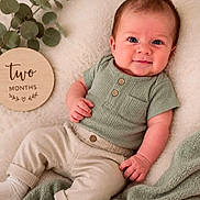 Bennett joined the competition — help win amazing prizes! baby, infant, two_months, smiling, green_top, beige_pants, socks, blanket, wooden_sign, milestone, plant, indoor, portrait, cute, young_child, lying_down, soft_texture, cozy, happy, face