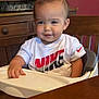 toddler, child, high_chair, white_shirt, nike_logo, smiling, indoor, wooden_furniture, table, plate, person, cute, baby, seated, face, short_hair, casual_clothing, kitchen, home, young_child